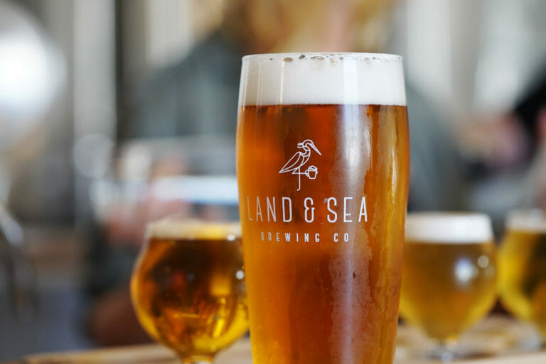 image of branded Land & Sea pint glass filled with beer, with a flight in the background