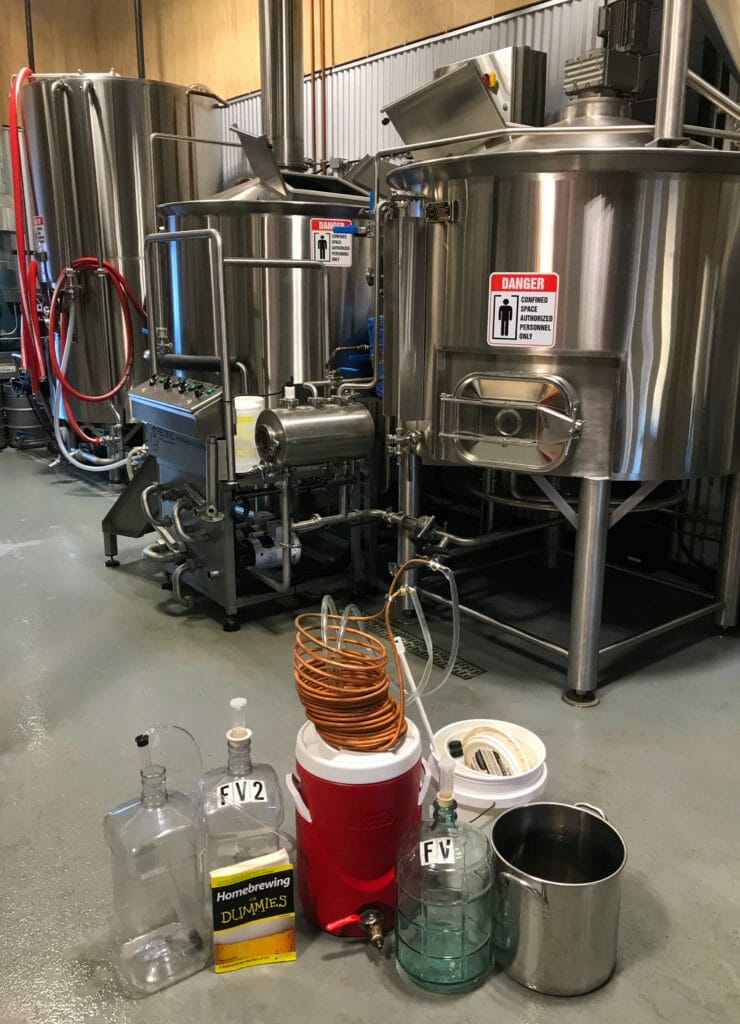 Some buckets and a copy of "Homebrewing For Dummies" in front of the stainless steel tanks of the brewery.