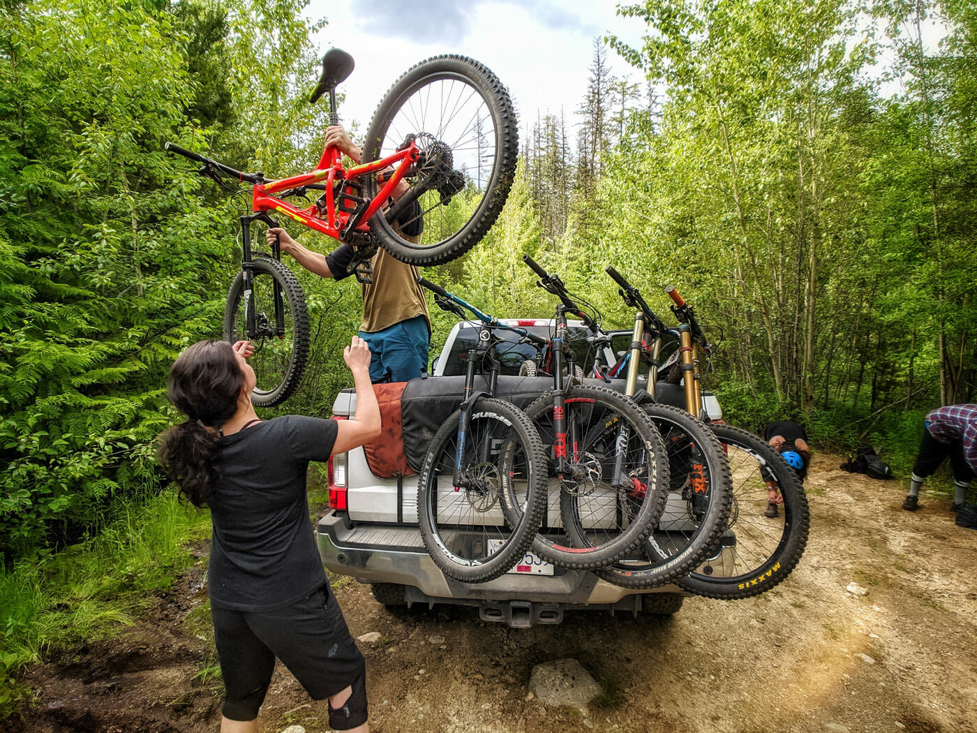 West Kootenay biking: Man hands mountain bike to woman from truck in the Merry Creek biking area in Castlegar, BC